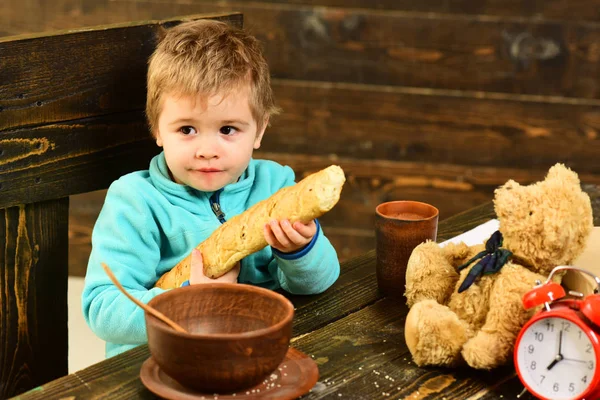 Niño con baguette francesa y osito de peluche en la mesa. Chico disfrutar de la cena con amigo juguete. Niño pequeño con pan fresco. Dale a tu cuerpo comida saludable como un niño bueno — Foto de Stock