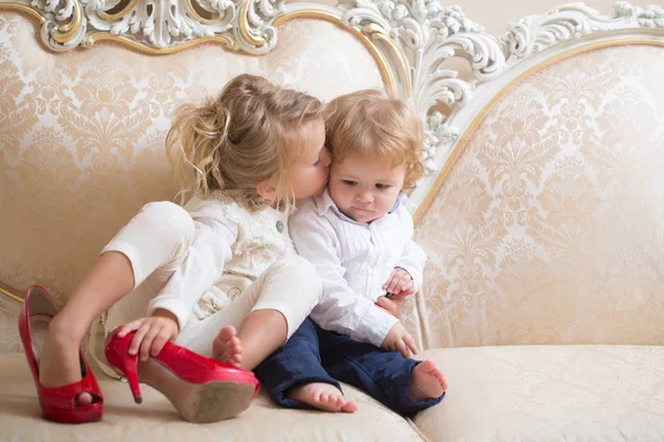 Сестра цілує брата з світлим волоссям на класичному дивані — стокове фото