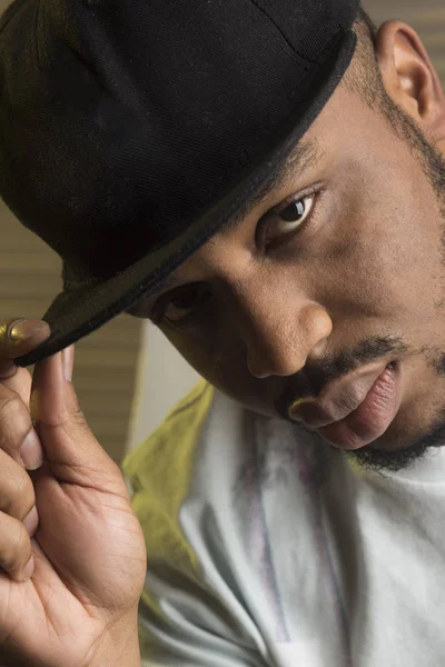 Rapero concepto de cultura. Negro macho con barba lleva gorra de rapero y se ve guapo. Hombre en la cara tranquila con grandes labios sensuales, de cerca. Hombre con barba y bigote interior, fondo jalousie — Foto de Stock