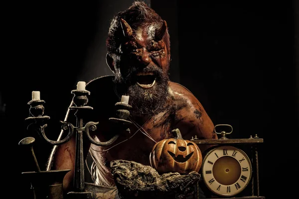 Halloween satan man with horns shout with pumpkin, clock, candlestick