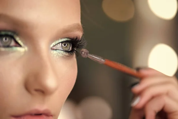 Frau trägt schwarze Wimperntusche mit Make-up-Pinsel auf. junge schöne Frau Mascara Make-up auf die Augen durch Pinsel auftragen. Schönheit Mädchen Make-up über grauem Hintergrund — Stockfoto