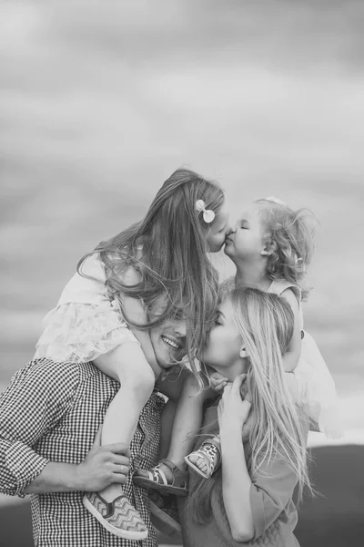 Девочки целуются на материнских плечах отца на облачном небе — стоковое фото