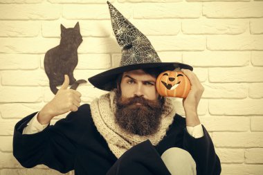 Cadılar Bayramı kötü büyü ve büyü. Katta oturan kabak ile cadı şapkalı adam. Sonbahar tatil kutlama. Kötü şans kavramı. Hipster başparmak duvar siyah kedi sembolü ile gösterilen.