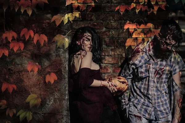 Pareja de Halloween de pie en la pared de ladrillo con hojas de otoño —  Fotos de Stock