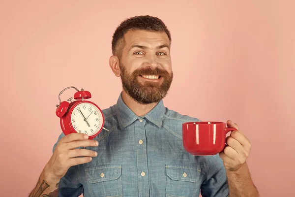 Hombre con barba en cara feliz con taza, despertador —  Fotos de Stock