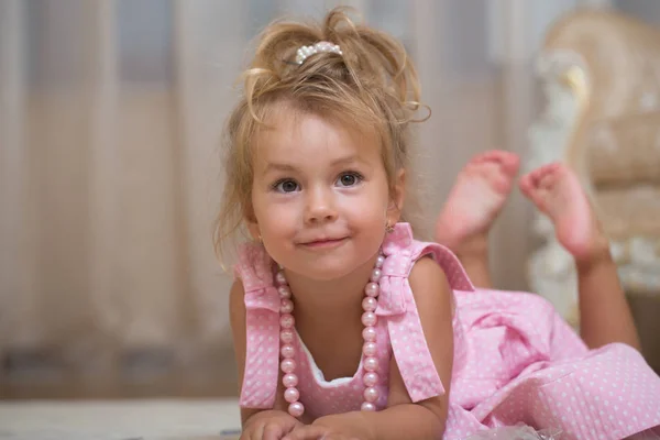 Menina bebê em vestido rosa, colar talão mentira no tapete — Fotografia de Stock