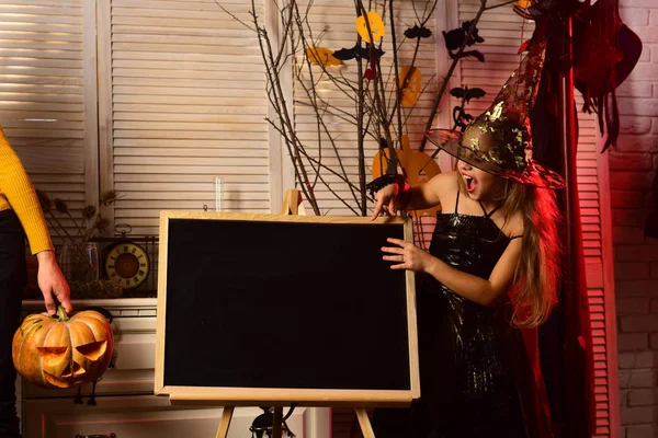 Feliz niño pequeño envidio a la fiesta de Halloween. Niña vestida para fiesta de disfraces apuntando a la pizarra. Feliz Halloween, brujas. Tengo la sensación de que esta noche va a ser una noche de abucheo, espacio para copiar —  Fotos de Stock