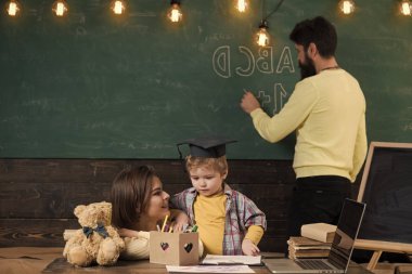 Çocuk Anne dikkat dinliyor. Evde eğitim kavramı. Aile hakkında akıllı küçük oğulları eğitim veriyor. Kara tahta arka plan baba yazar iken zeki oğlu, annesi öğretir.