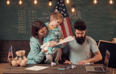 Evde eğitim kavramı. Resepsiyon ile kağıt uçak yapma evlat, Amerikan ailesi. Ebeveynler sınıf ABD bayrağı ile kara tahta arka plan ile evlat. Anne oğlu Amerikan gelenekleri oynarken öğretim.