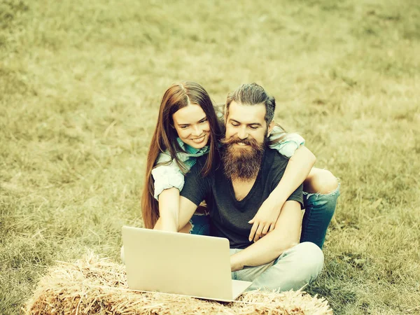 Chica o mujer feliz y hombre barbudo usando el ordenador portátil en la naturaleza —  Fotos de Stock
