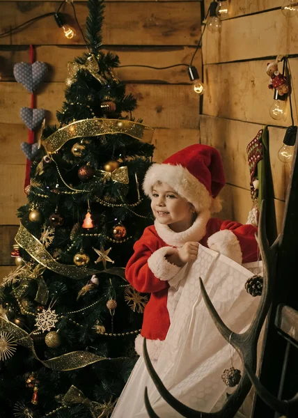 Weihnachtsfeier. Winterurlaub und Urlaub. Neujahr kleines Mädchen mit Hut. Weihnachtsglückliches Kind mit Weihnachtsmann am Weihnachtsbaum. — Stockfoto