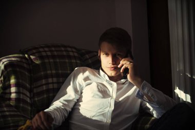 Beyaz tişörtlü adam konuşmak üstünde hareket eden telefon içinde koltuk