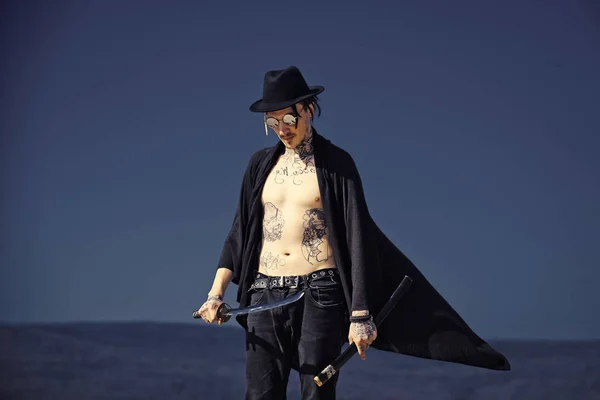 Воин в черной шляпе и открытой одежде с татуированным туловищем — стоковое фото