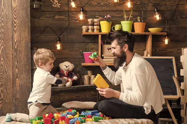 家庭在家里玩构造函数。爸爸和孩子玩玩具车, 砖块。背景上有玩具和黑板的托儿所。父亲和快乐的儿子玩构造器。父理念. — 图库照片