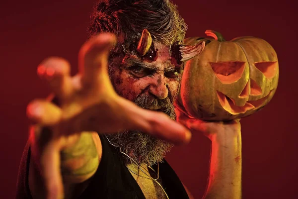 Halloween hombre diablo mantenga calabaza sobre fondo rojo — Foto de Stock