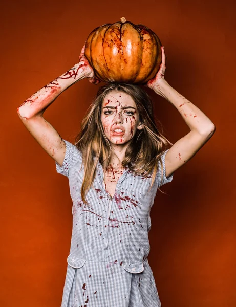 Halloween dziewczyna z rzeźbione dyni. Portret kobiety z tworzą krwi na jej twarzy. Sexy kobieta nosić niebieski drees z krwi. Ona ma dyni trzyma w ręce nad głową. — Zdjęcie stockowe