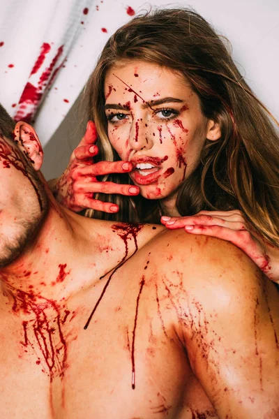 Terrible pareja de zombies. La sangre fluye por el cuello, las marcas de mordeduras son visibles. Un terrible episodio de Halloween, la chica muerde a su novio por el cuello, con sangre en la cara y sed de sangre . —  Fotos de Stock