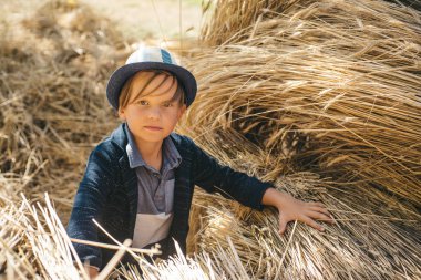 Köyde sonbahar tatiline çıkmış tatlı bir çocuk. Çocuk sonbahar için çocuk kıyafetleri reklamı yapıyor. Kafasında samanlıkta şapka olan neşeli bir adam. Mutlu çocukluk.