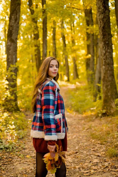 秋季大减价美丽的笑容可亲的女孩,一头长发,穿着时髦的夹克,在秋日装扮.秋天的肖像微笑的女人在公园里拿着黄色的枫叶. — 图库照片