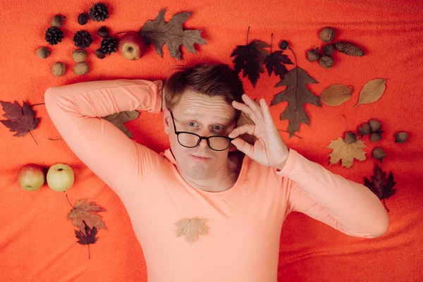 Hombre pelirrojo jugando con hojas y mirando a la cámara. Retrato de moda de hermoso hombre sensual en jersey. Hombre divertido en traje descansando con hojas se encuentra en el suelo de madera en hojas de otoño . —  Fotos de Stock