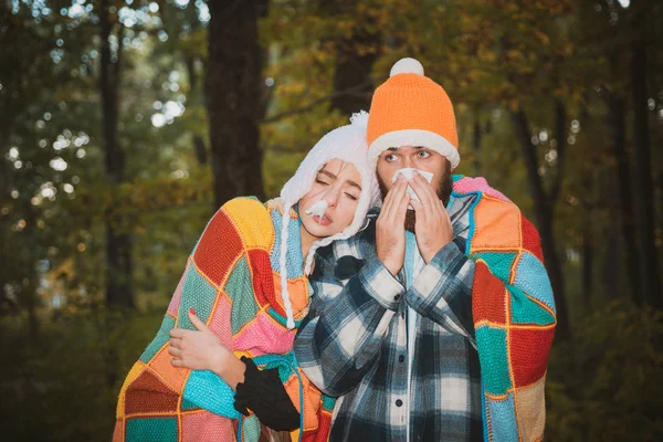 Es zeigt ein krankes Paar, das im Herbstpark niest. Mädchen mit Taschentuch und niesender Junge im Herbstpark. Kranke Paare erkälten sich. Ein krankes Paar versucht, in die Serviette zu niesen. Grippeepidemie stoppen — Stockfoto