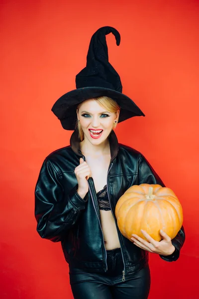 かぼちゃの赤い背景の上にハロウィーンの衣装で感情的な若い女性。魔女のかぼちゃのポーズ. — ストック写真