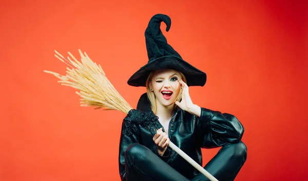 Bruxa segurando vassoura ou vassoura. onça mulheres em preto bruxa halloween trajes em festa sobre fundo vermelho. Jovem gótica feliz em traje de bruxa halloween . — Fotografia de Stock