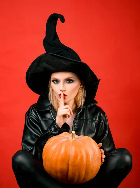 赤い背景のパーティーで黒魔女ハロウィンの衣装を着た若い女性。魔女ポージングとカボチャ. — ストック写真