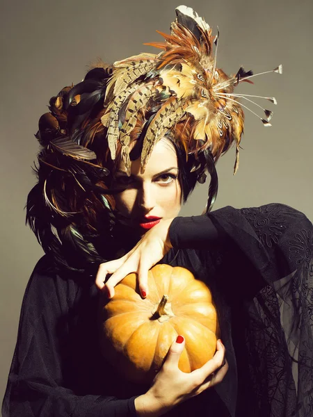 Hezká žena v klobouku peří drží halloween dýně — Stock fotografie