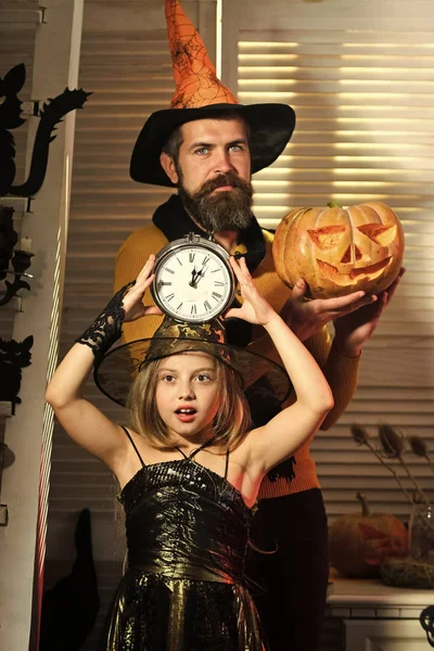 Wizard and little witch in hats hold clock and pumpkin.