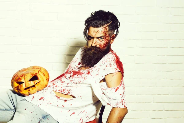 Halloween zombie bearded man with pumpkin in red bloody shirt