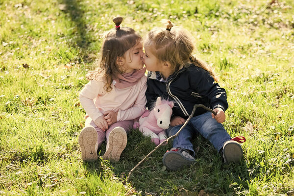 Boy and girl sit on green grass. Brother and sister kiss on sunny day. Kids play with stick and toy horse. Family, love, trust. Children, childhood concept.