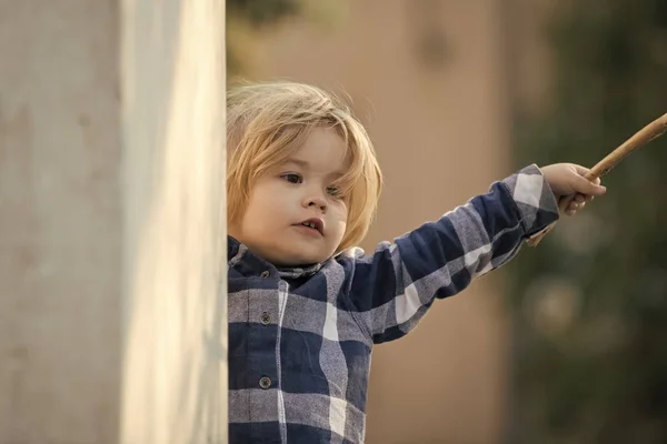 Niño con el pelo rubio en camisa a cuadros azul con palo — Foto de Stock