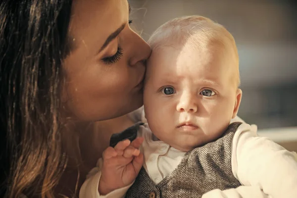 Mulher beijo bebê menino com olhos azuis no rosto bonito — Fotografia de Stock
