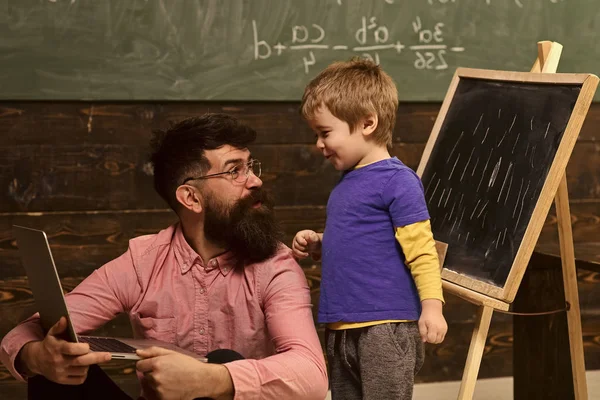 Otec a syn v učebně. Boční pohled muž a dítě na sebe dívali s pobavením. Chlap v růžové košili na podlaze s notebookem — Stock fotografie