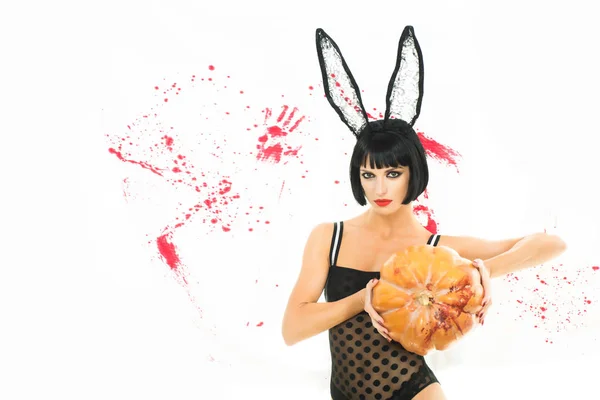 Jolie femme vêtue de lapin habillé de citrouilles. Sexy zombie fille tenant une citrouille sur fond blanc sanglant. Halloween maquillage belle femme . — Photo