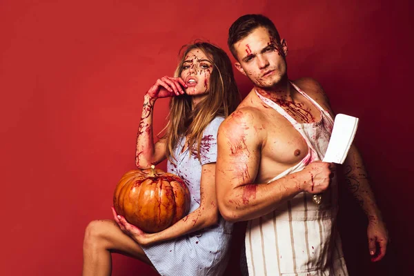 Zombie pár rozhalenou člověka a upíra žena krev a halloween make-up drží dýně. Izolované na červeném pozadí. Modely s krvavou rukou a krev na obličeji. — Stock fotografie