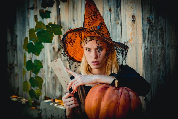 Μάγισσα κορίτσι ετοιμάζεται να κόψει μια κολοκύθα σε ξύλο φόντο. Έννοια του Halloween. Close-up πορτρέτο της πανέμορφη ξανθιά νεράιδα. — Φωτογραφία Αρχείου
