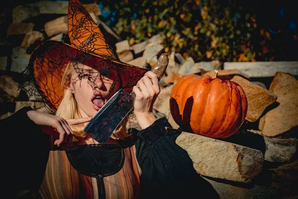 Chica modelo atractiva en disfraz de Halloween. Chica preparándose para cortar una calabaza. Bruja en el sombrero de Halloween posando al aire libre. Concepto de Halloween . — Foto de Stock