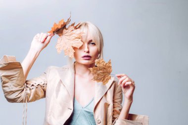 Yaprakları ile oynama ve kameraya arıyorum sürpriz kadın. Kız sonbahar sonbahar yaprakları arka plan üzerinde yaprakları ile oynarken. Sarı zemin üzerine altın varak tutan güzel seksi genç kadın.