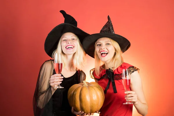 Laughing funny sister twins girls in witches costumes in halloween. Two happy young women in black and red dresses, costumes witches halloween on party over orange background. Halloween copy space.