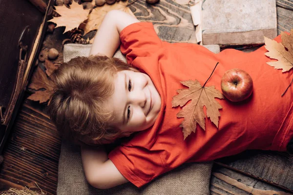 Kid har kul med blad falla. Leende liten pojke klädd i fashionabla säsongsbetonade kläder med höstlig stämning. Kid spelar under hösten. Söt liten barn pojke är redo för hösten. — Stockfoto