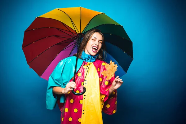 Vonzó fiatal nő a szezonális ruhák a golden leaf. Eladó hihetetlen kedvezmények teljes őszi kollekció. Gyönyörű nő csodálatos szivárvány színű esernyő elszigetelt kék háttér. — Stock Fotó