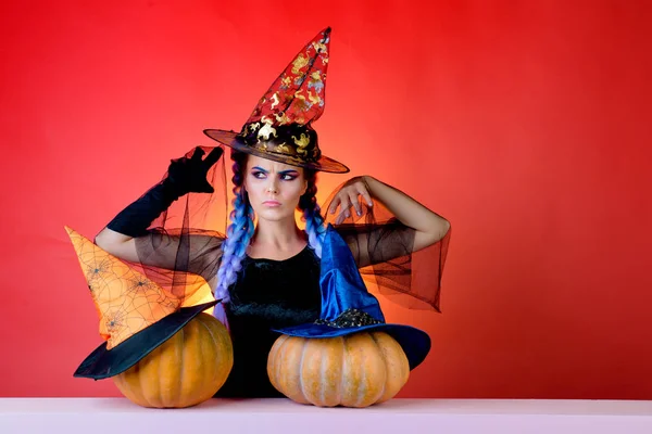 Hermosa joven con traje de bruja negra con sombrero de pie sobre fondo rojo. Feliz joven con disfraz de bruja de Halloween en la fiesta sobre un fondo aislado. Las mejores ideas para Halloween . —  Fotos de Stock