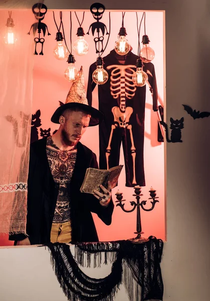 Hombre de Halloween con sonrisa sobre fondo oscuro. Brujo malvado con pelo rojo y barba en capa negra leyendo el libro de hechizos. 31 de octubre. Maquillaje y concepto de miedo para el hombre. Fiesta de celebración . —  Fotos de Stock