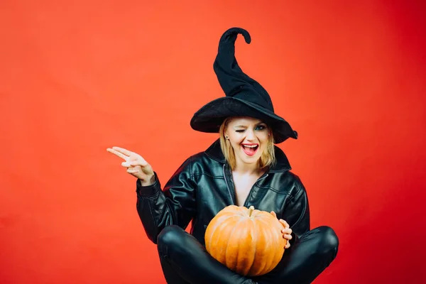 Visage drôle et femme surprise. jeunes femmes motionnelles en costumes d'Halloween sur la fête sur fond rouge avec citrouille. Sorcière posant à la citrouille . — Photo