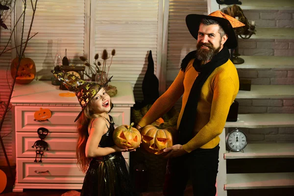 Wizard and little witch in hats hold jack o lanterns