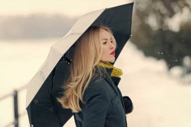 Tatil kutlama kavramı. Gri ceket, atkı ve eldiven modeli. Kız şemsiye ile kış gününde yürüyüş. Noel ve yeni yıl. Beyaz kar manzara üzerinde uzun sarı saçlı kadın.