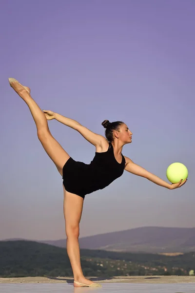 Vrouw gymnast in zwarte sportkleding met groene bal in split — Stockfoto