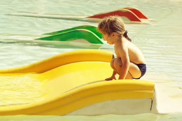 Feliz menino bonito joga no slide de água amarelo — Fotografia de Stock